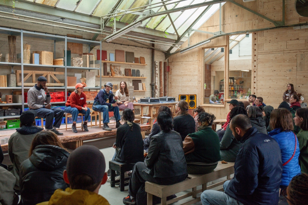 People sitting in front of a small stage where a panel of 4 people is sitting
